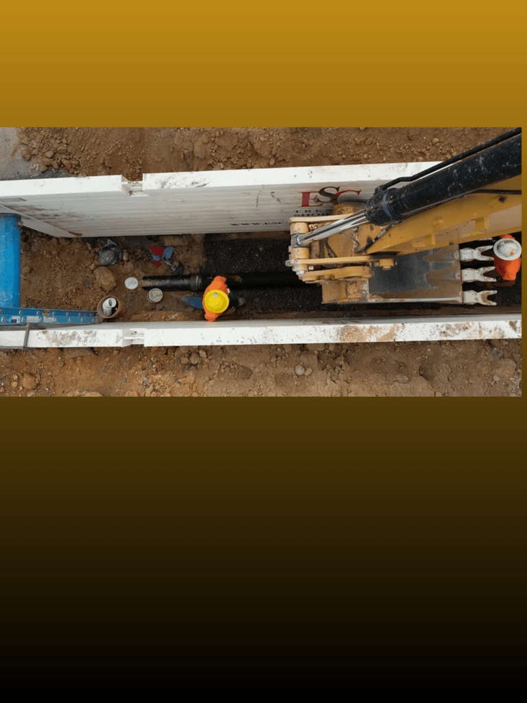 Construction crew working safely inside a protected trench using a trench box, ladder access, and proper PPE.
